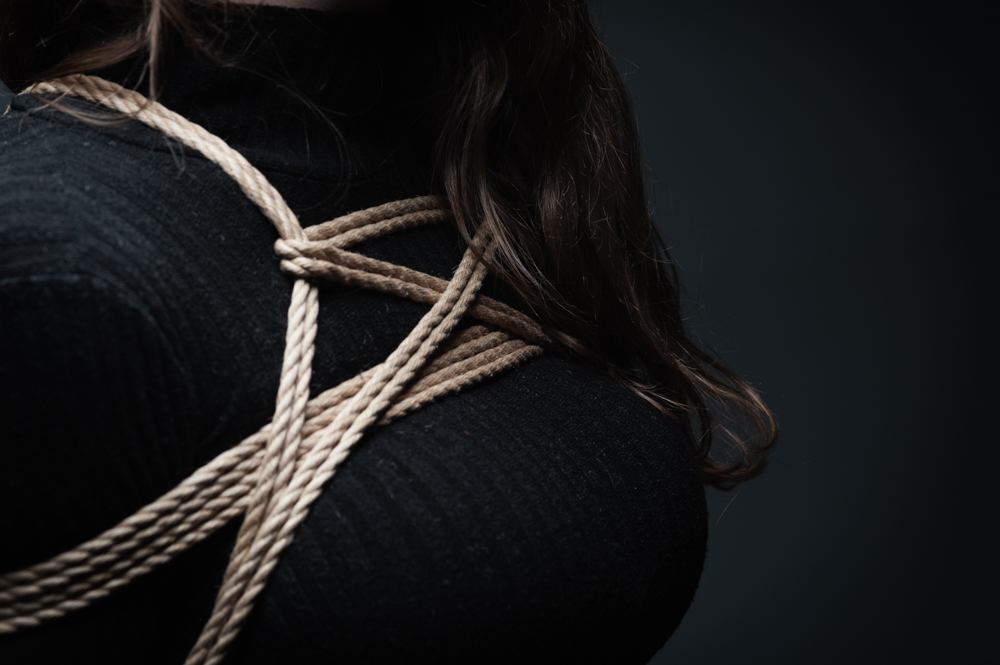 A woman in a black ribbed shirt tied in a box tie. Framed in tight, showing the rope.